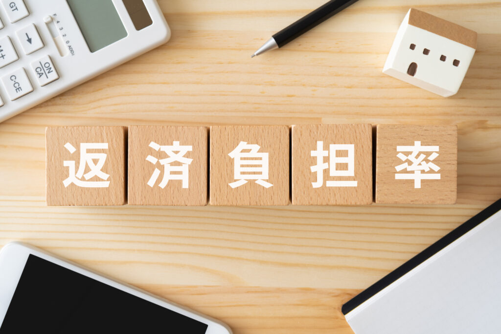 ②返済負担率と書かれたブロック、電卓、家の模型、スマホ、ノート